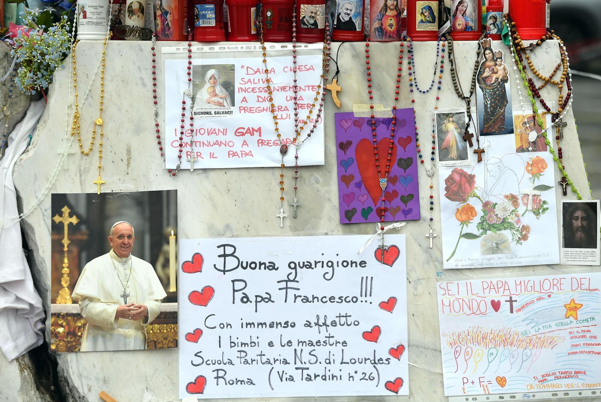 Velas, rosarios y mensajes de apoyo al papa Francisco se exhiben en la estatua del papa Juan Pablo II junto al Hospital Universitario Gemelli.