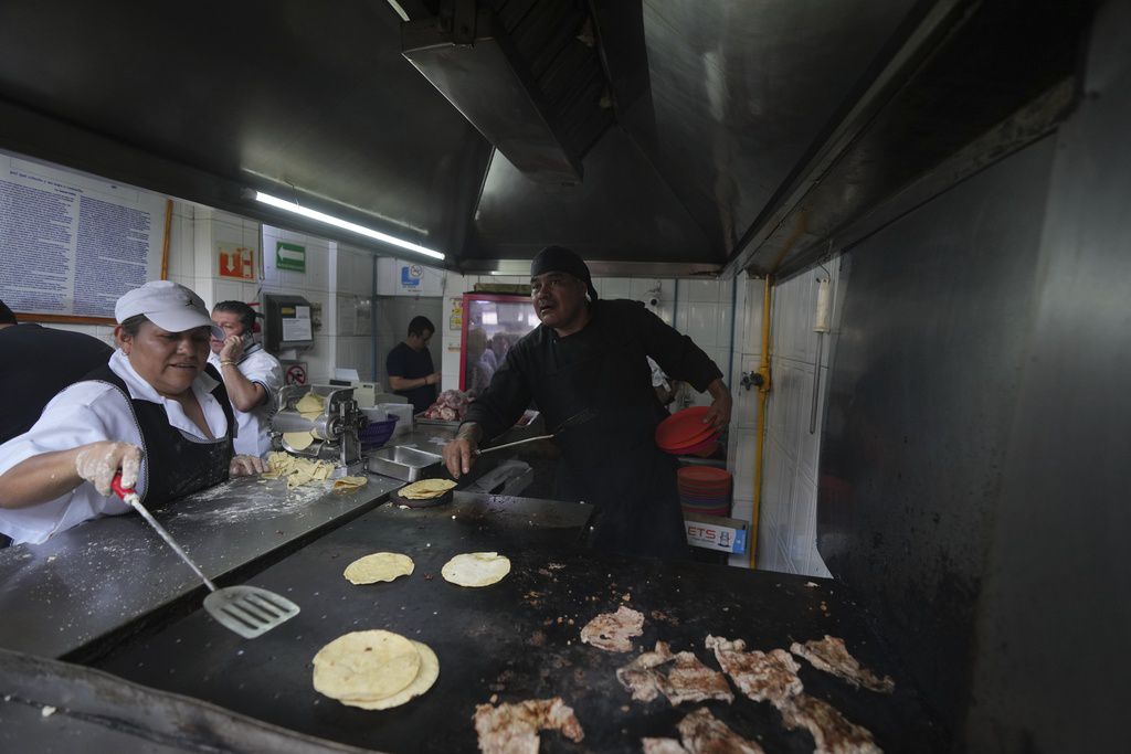 El chef Arturo Rivera Martínez, recién galardonado con una estrella Michelin, agarra varios platos mientras una ayudante calienta las tortillas de maíz en una plancha en la taquería Tacos El Califa de León en Ciudad de México.
