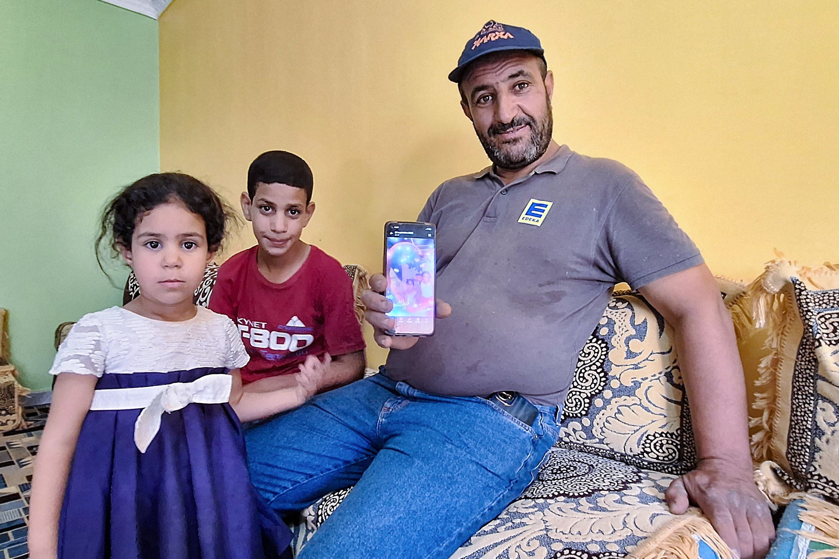 Omar Khelif, padre de la boxeadora argelina Imane Khelif, muestra una foto de su hija cuando era niña mientras está sentado acompañado de sus dos hijos pequeños en la casa familiar en la provincia de Tiaret el 2 de agosto de 2024. (Foto: AFP)