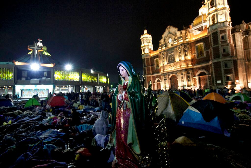 Una estatua de la Virgen de Guadalupe está junto a peregrinos dormidos mientras esperan la misa afuera de la Basílica de Guadalupe en la Ciudad de México. 