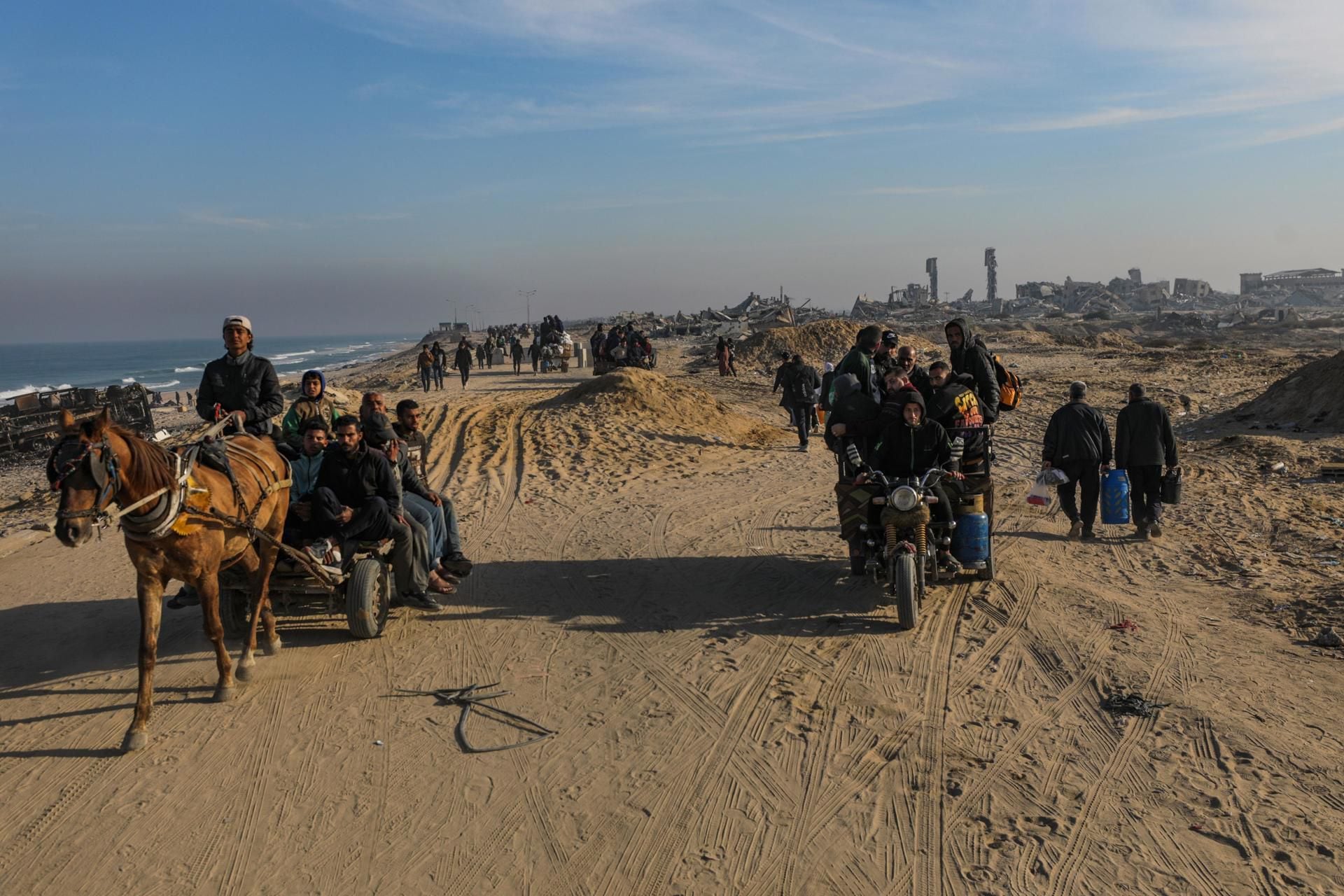 Familias palestinas caminan entre los escombros en el camino Al Rashid, luego de que Israel acordara el alto al fuego en Gaza.