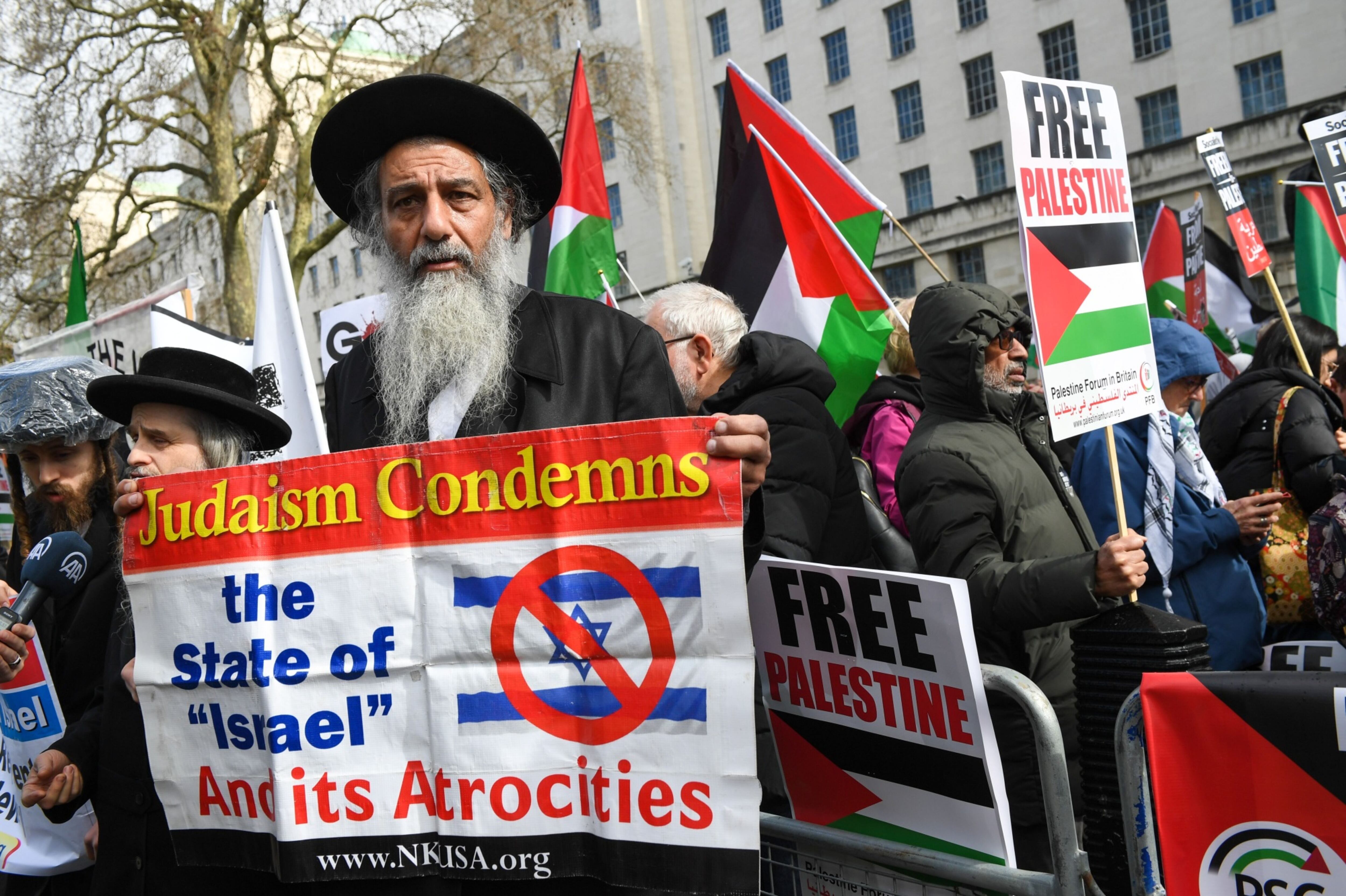 Un judío ortodoxo sostiene una pancarta que dice 'El judaísmo condena el Estado de Israel y sus atrocidades' mientras los manifestantes ondean banderas palestinas durante una manifestación.