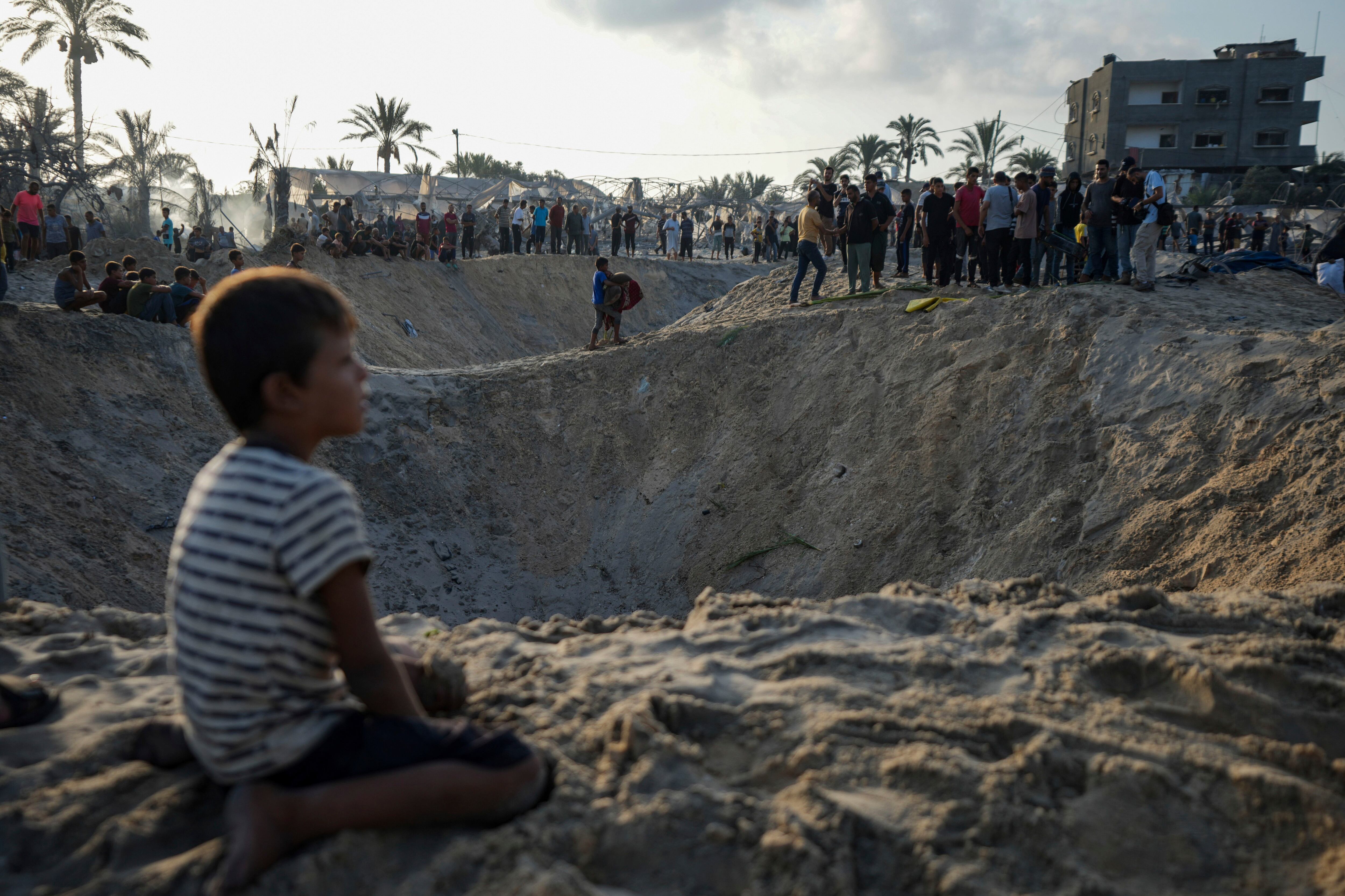 Palestinos observan la destrucción causada por un bombardeo israelí contra un campamento de desplazados por la guerra, en Muwasi, Gaza.