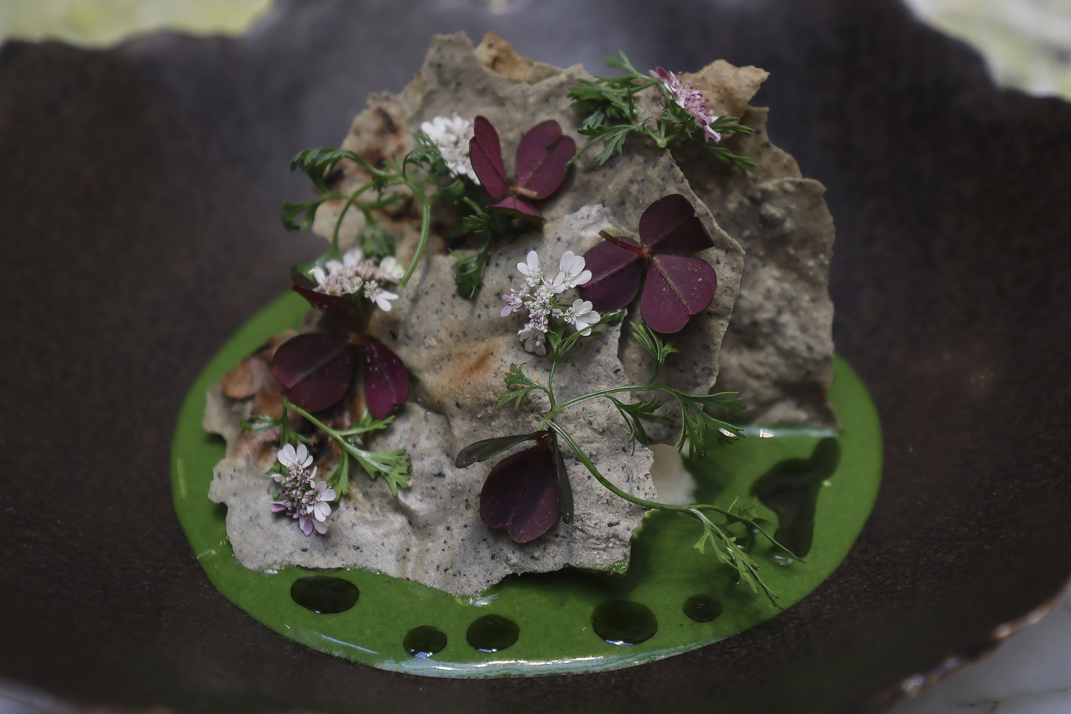 Un plato de cangrejo moro en pipián verde de semillas de girasol, lima tailandesa y albahaca con tostadas de maíz azul y flores, en el restaurante Quintonil, en la Ciudad de México, el 28 de febrero de 2025. (AP Foto/Ginnette Riquelme)