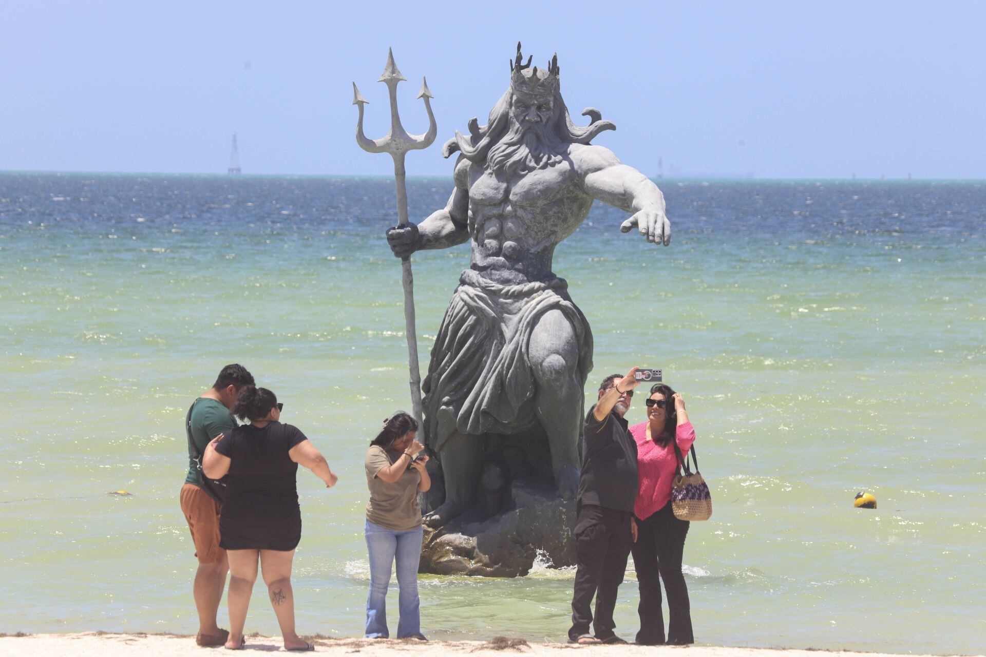 Turistas locales e internacionales visitan la estatua de Poseidón instalada en la playa de Puerto Progreso. 