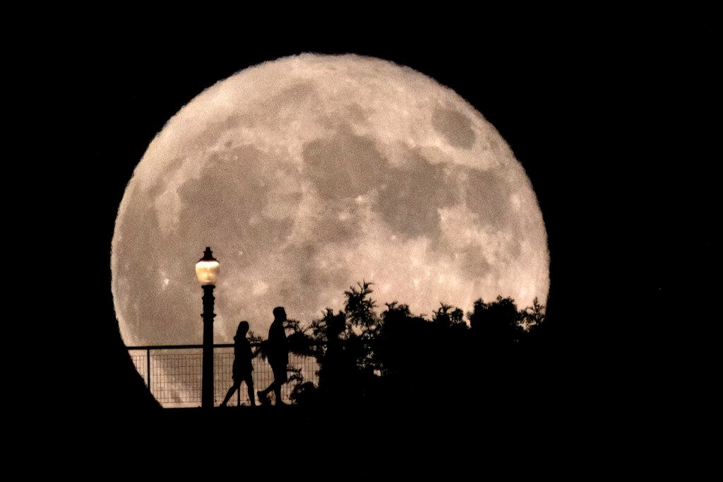 Un grupo de personas camina delante de una superluna creciente en el Observatorio Griffith de Los Ángeles. (AP)