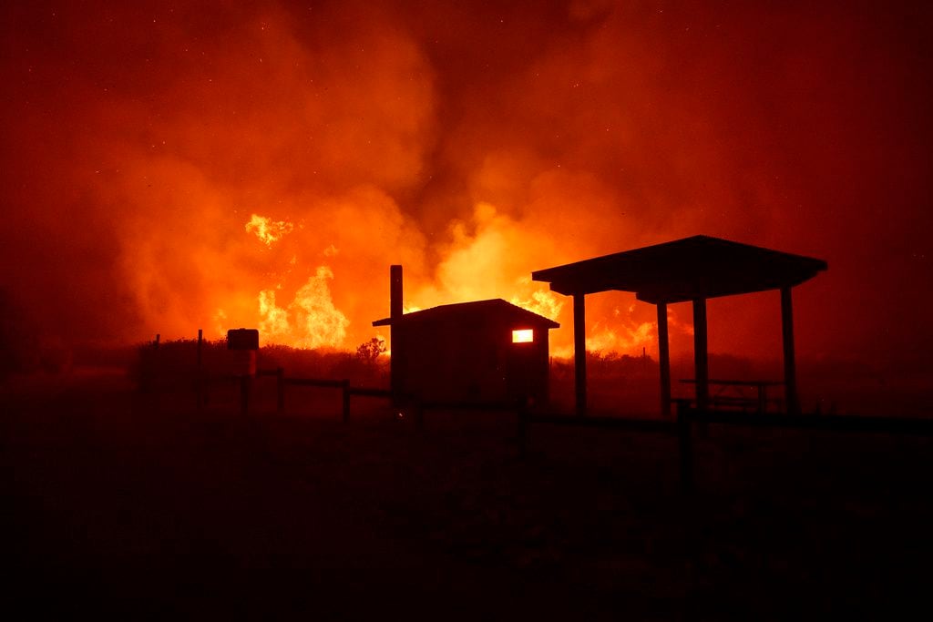 Las llamas de un incendio forestal se acercan a unas estructuras.